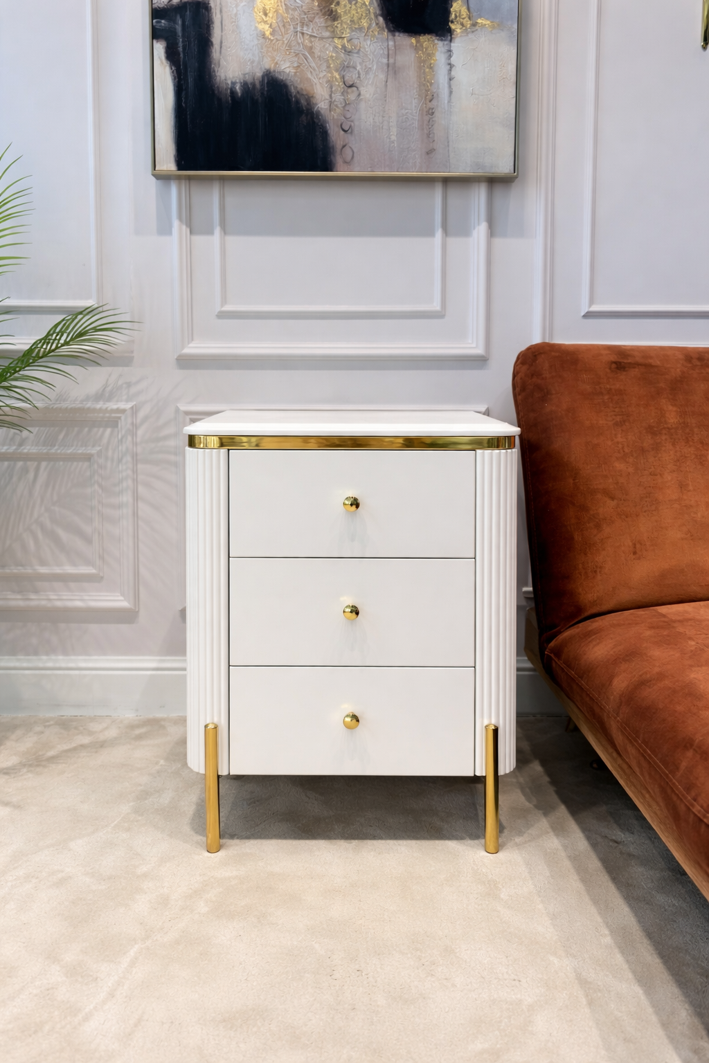SZAFKA NOCNA Anne biały korpus z pionowymi ryflowaniami, złote błyszczące elementy, blat z konglomeratu marmurowego na nóżkach